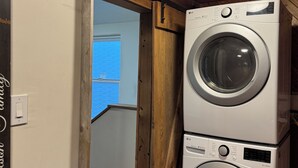 Lavanderia con due lavatrici a carica frontale LG impilate, soffitto in legno e una porta che dà su un'altra stanza.
