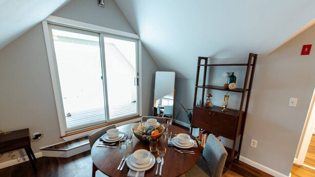 A dining area with a round table set for four, a wooden bench, and a bookshelf with decorative items. - Cozy Loft steps from VT Downtown (Bennington)