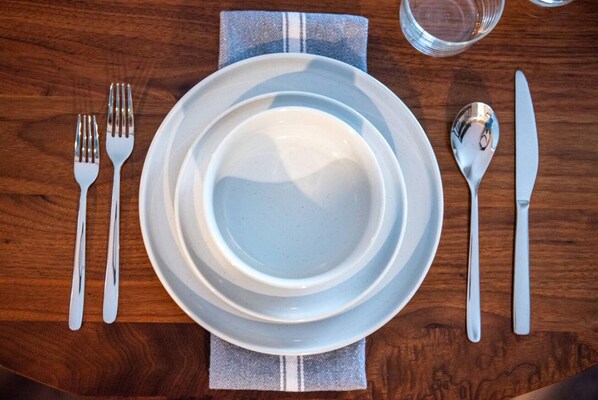 A table set with white plates, forks, knives, and spoons on a wooden table. - Cozy Loft steps from VT Downtown (Bennington)