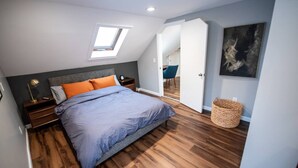 A bedroom with a bed, a nightstand, a lamp, a window, a door, and a wall-mounted artwork. - Cozy Loft steps from VT Downtown (Bennington)