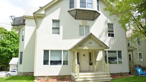 A two-story building with a white exterior, a front porch, and a number '124' displayed above the entrance. - Cozy Loft steps from VT Downtown (Bennington)