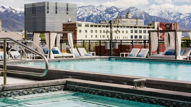 A pool area with lounge chairs and a view of snow-capped mountains in the background. - Convention Ctr Luxury 1BR Pool Gym Hot Tub (Salt Lake City)