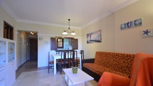 A living room with a sofa, a dining table with chairs, a kitchen area, and a hallway.