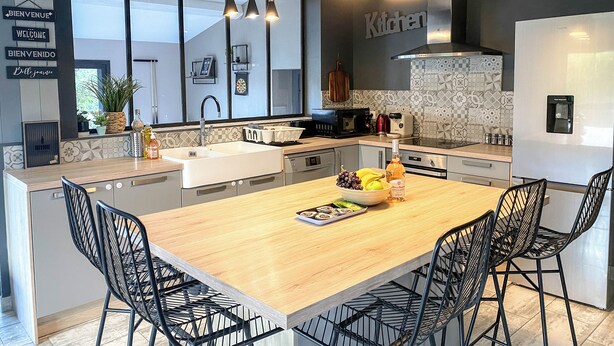 A modern kitchen with a large island, black chairs, and a variety of appliances. - Carcalove - Pool, Billiards & Jacuzzi - 10pax (Fontiès-d'Aude)