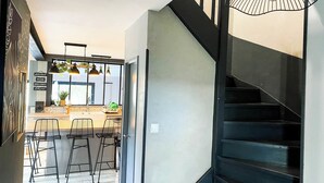 A modern kitchen with bar stools, a staircase, and a hanging light fixture. - Carcalove - Pool, Billiards & Jacuzzi - 10pax (Fontiès-d'Aude)