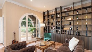 Een ruime woonkamer met een uitgebreide wijncollectie op planken, een groene fauteuil en een schaakbord op een houten tafel.