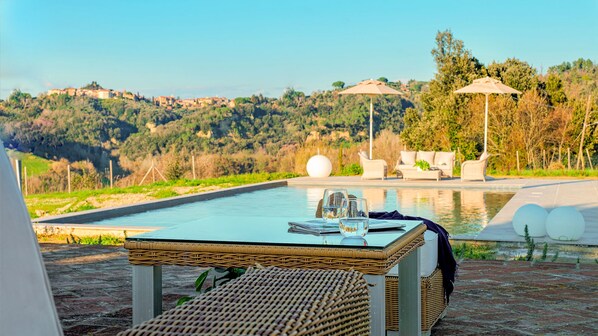 A poolside area with a table, chairs, and umbrellas.