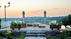 A terrace with outdoor furniture, a table, and two umbrellas, overlooking a scenic landscape.