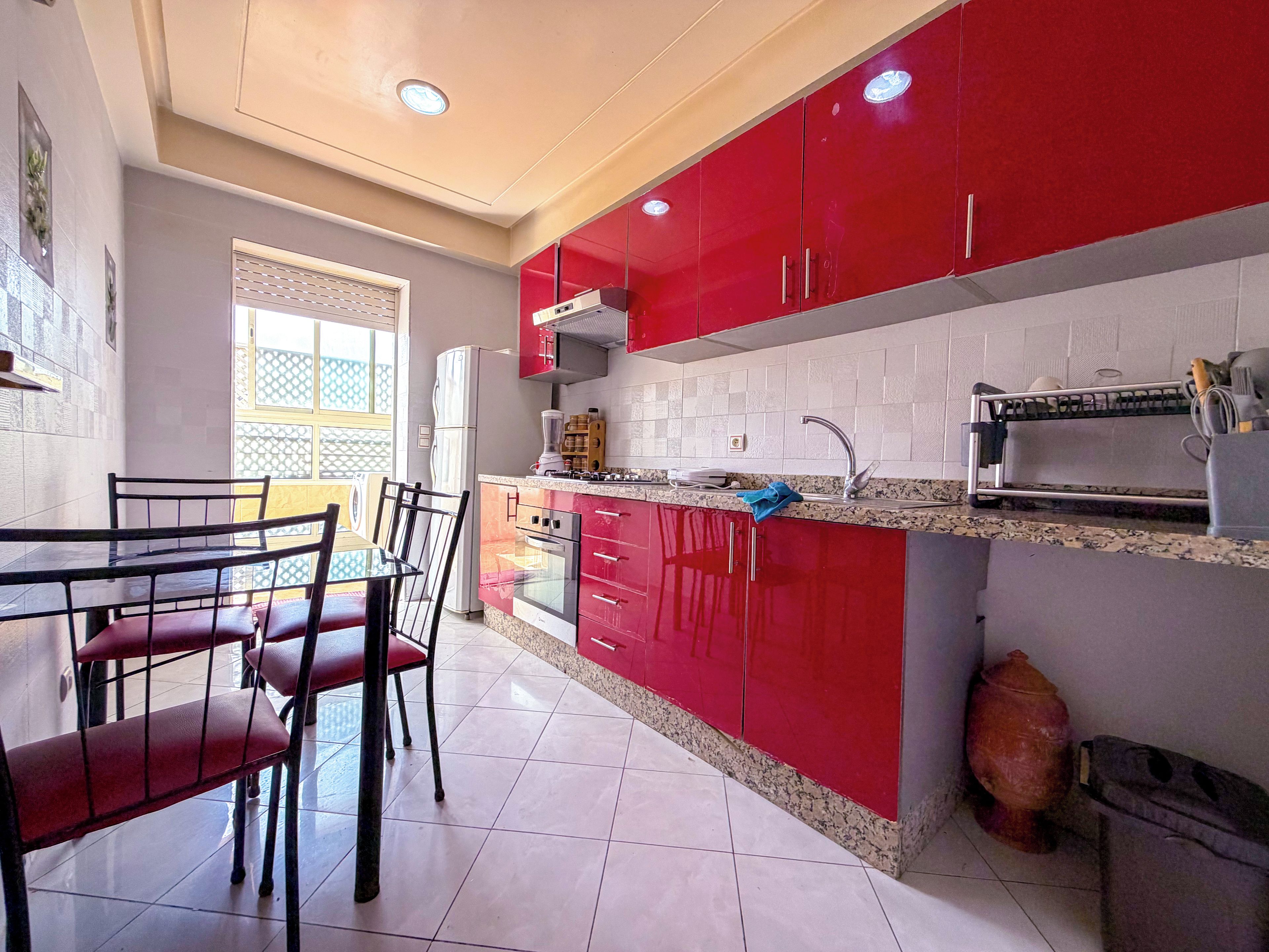 A kitchen with red cabinets, a granite countertop, and a dining area with chairs.