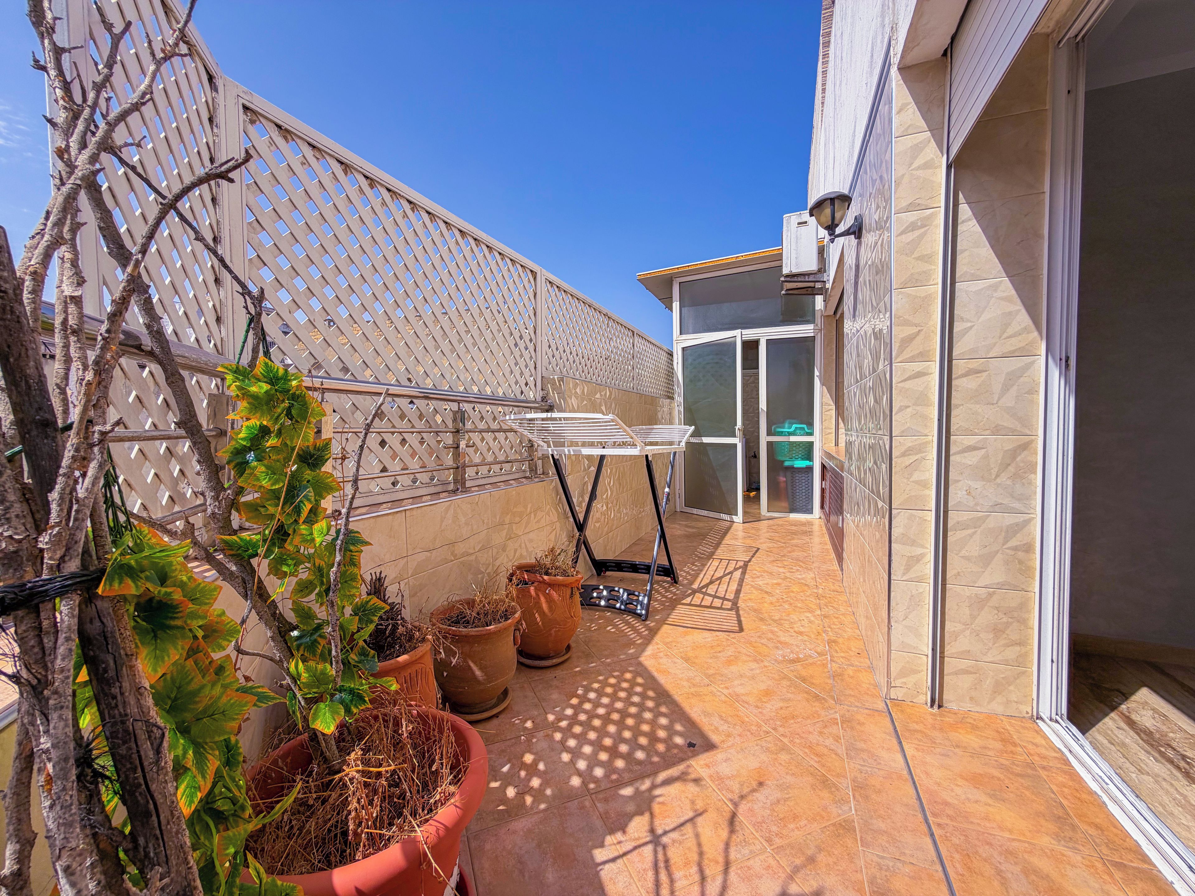 A balcony with potted plants, a drying rack, and a sliding glass door leading to a covered area.
