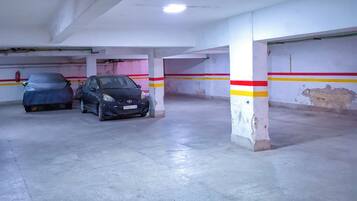 Een parkeergarage met twee geparkeerde auto's, betonnen pilaren en een plafondlamp.