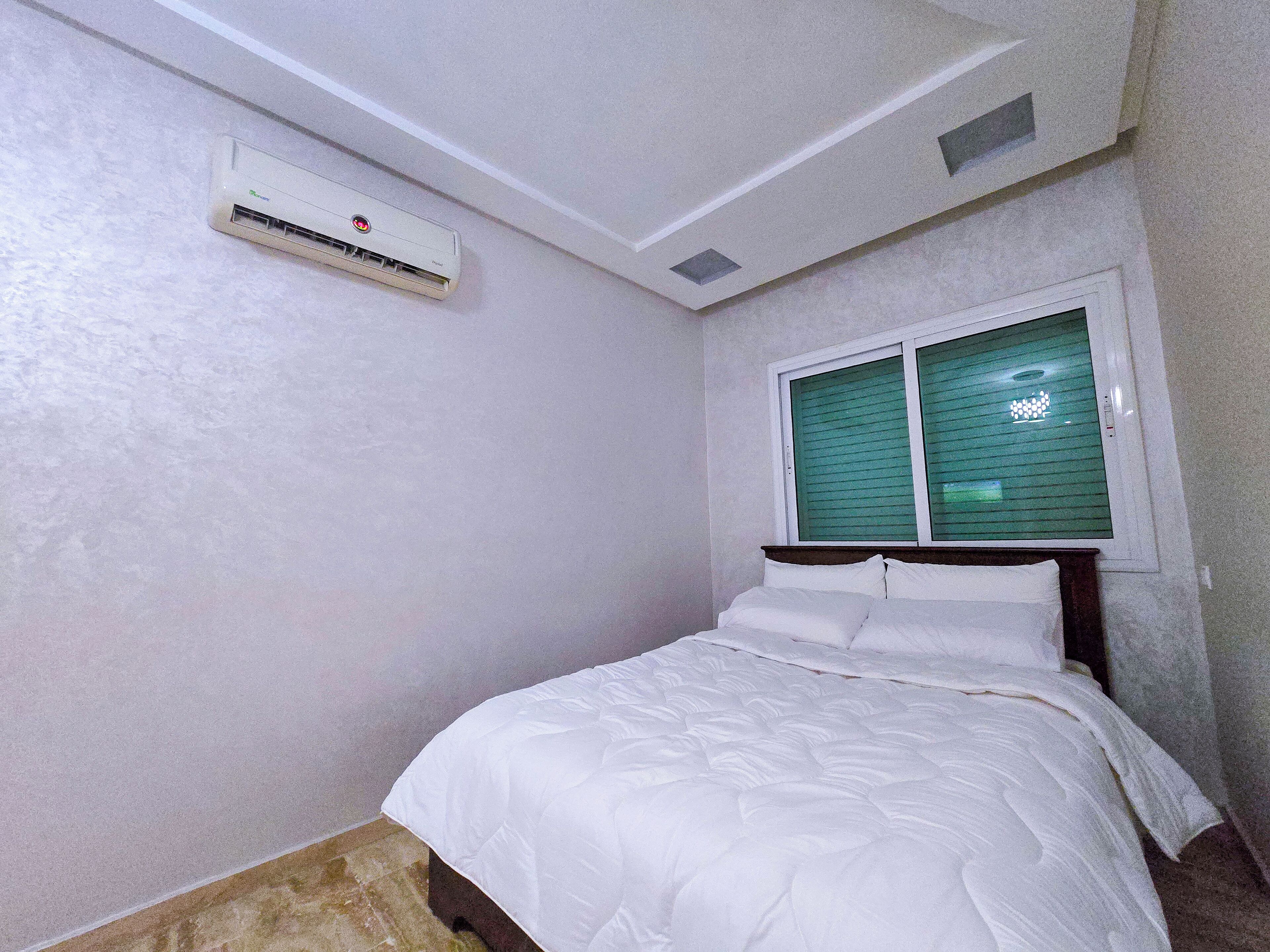 Een slaapkamer met een bed, een raam met zonwering, een airconditioning en een klein dakraam.