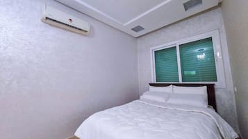 Een slaapkamer met een bed, een raam met zonwering, een airconditioning en een klein dakraam.