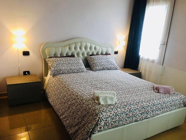 A neatly made bed with a floral-patterned bedspread, two pillows, and a bedside table with a lamp.