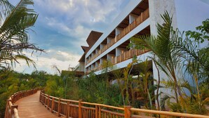A wooden boardwalk leading to a multi-story building with balconies, surrounded by lush greenery. - Hotel Mundo Maya Nuevo Uxmal (Santa Elena)