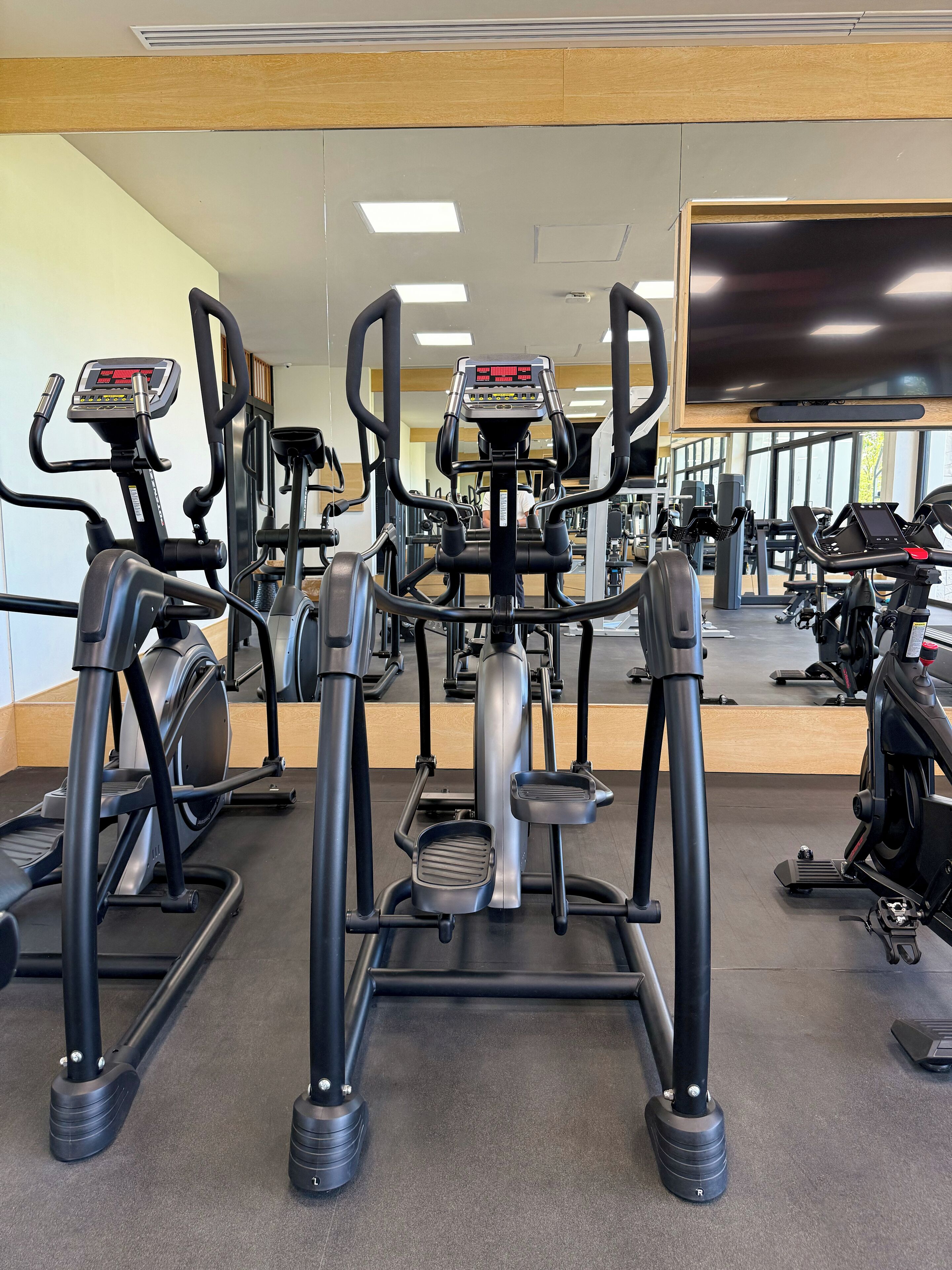 Een sportschool met diverse fitnessapparaten, waaronder loopbanden en elliptische trainers, gerangschikt in rijen.