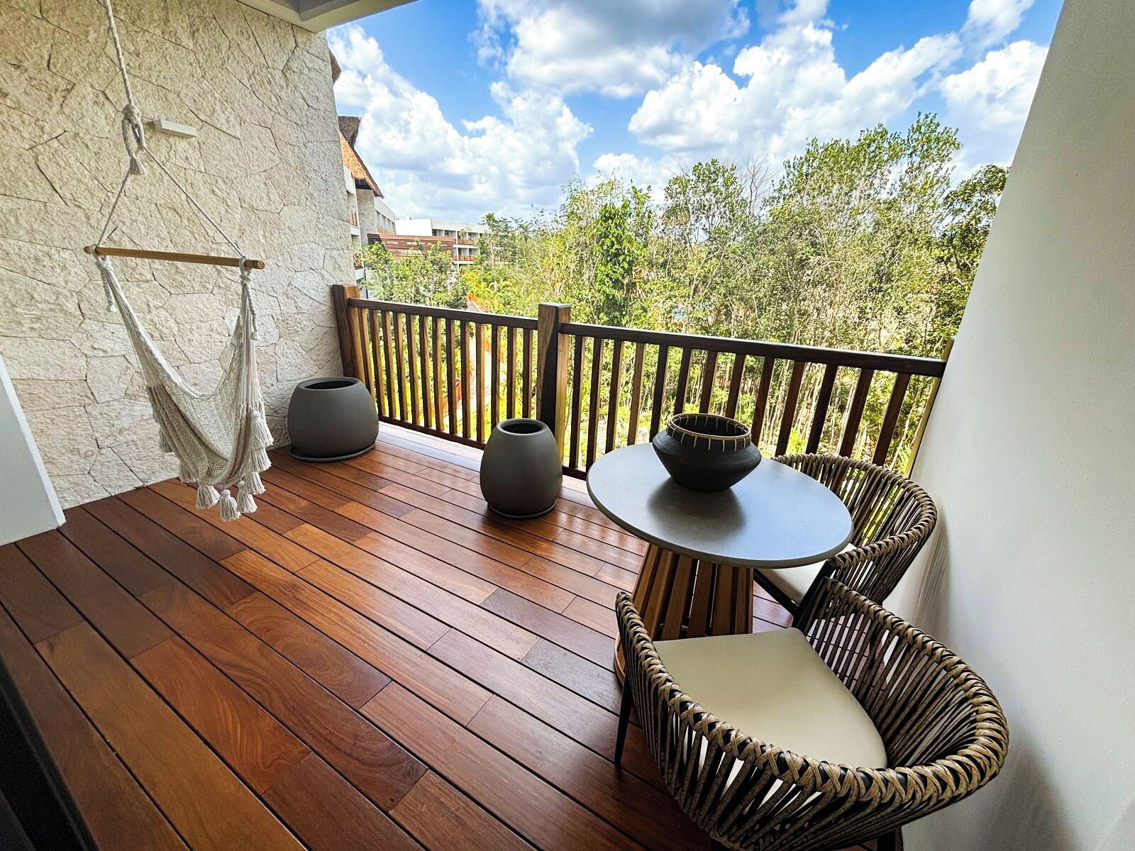 A wooden deck with a hammock, two planters, and wicker chairs.