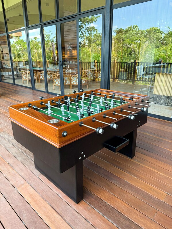 Una mesa de fútbol de mesa en una terraza de madera, con puertas de vidrio que dan a una zona de estar al aire libre.