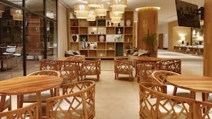A modern interior with round wooden tables and chairs, a central wooden column, and a ceiling with hanging wicker lamps. - Hotel Mundo Maya Nuevo Uxmal (Santa Elena)