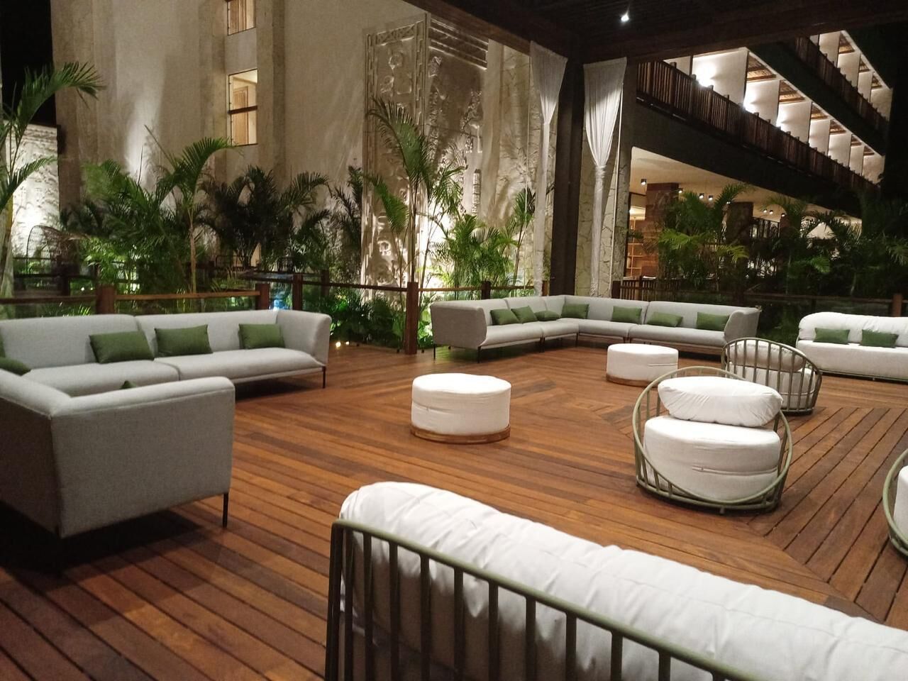 A spacious indoor area with a wooden floor, white sofas with green cushions, and a large staircase.