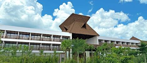 A resort with a large building featuring a unique thatched roof structure, a spacious outdoor area with a curved pathway, and lush greenery surrounding the property.