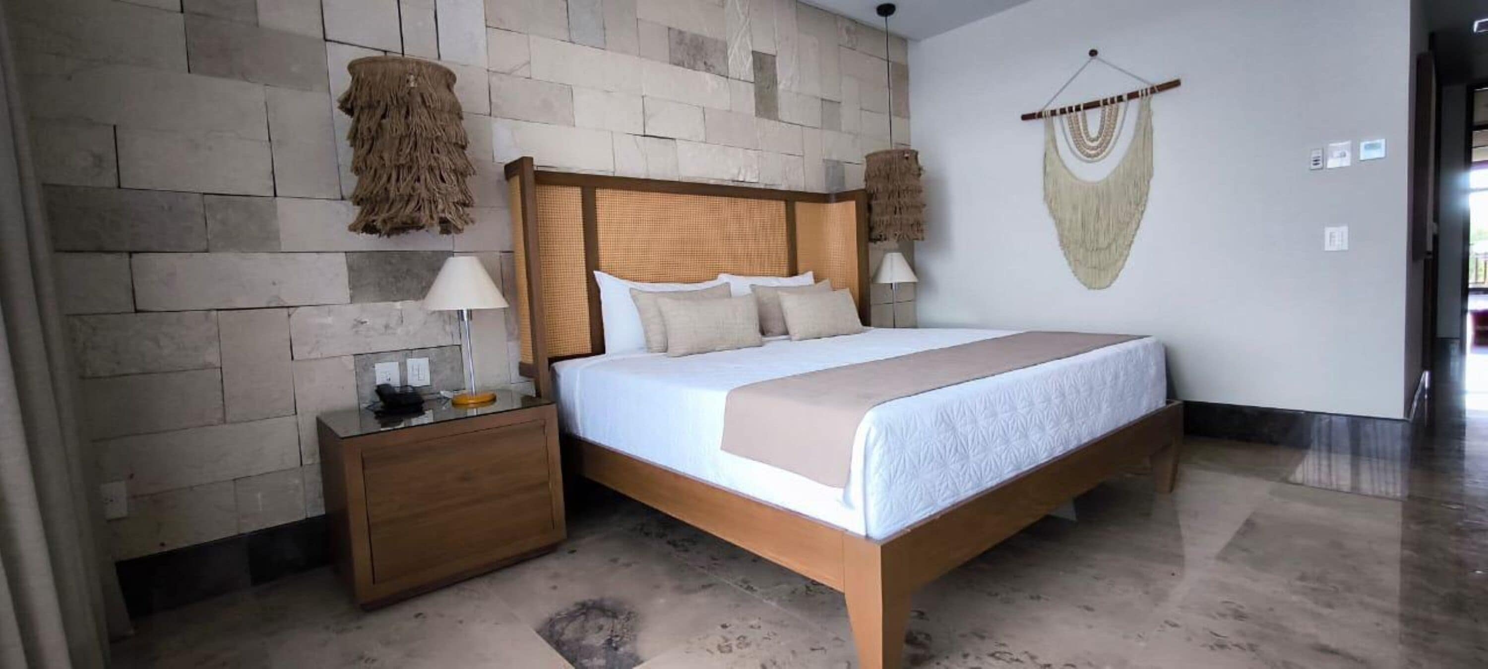 Une chambre avec un lit en bois, une table de chevet, une lampe fixée au mur et une décoration murale tissée.