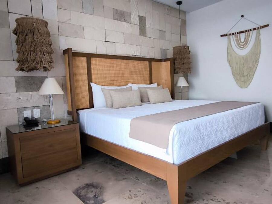 Quarto com cama de madeira, mesa de cabeceira, luminária na parede e tapeçaria na parede.