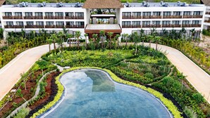 A resort with a large central pool surrounded by lush landscaping, a multi-story building with a distinctive thatched roof, and a view of distant hills. - Hotel Mundo Maya Nuevo Uxmal (Santa Elena)