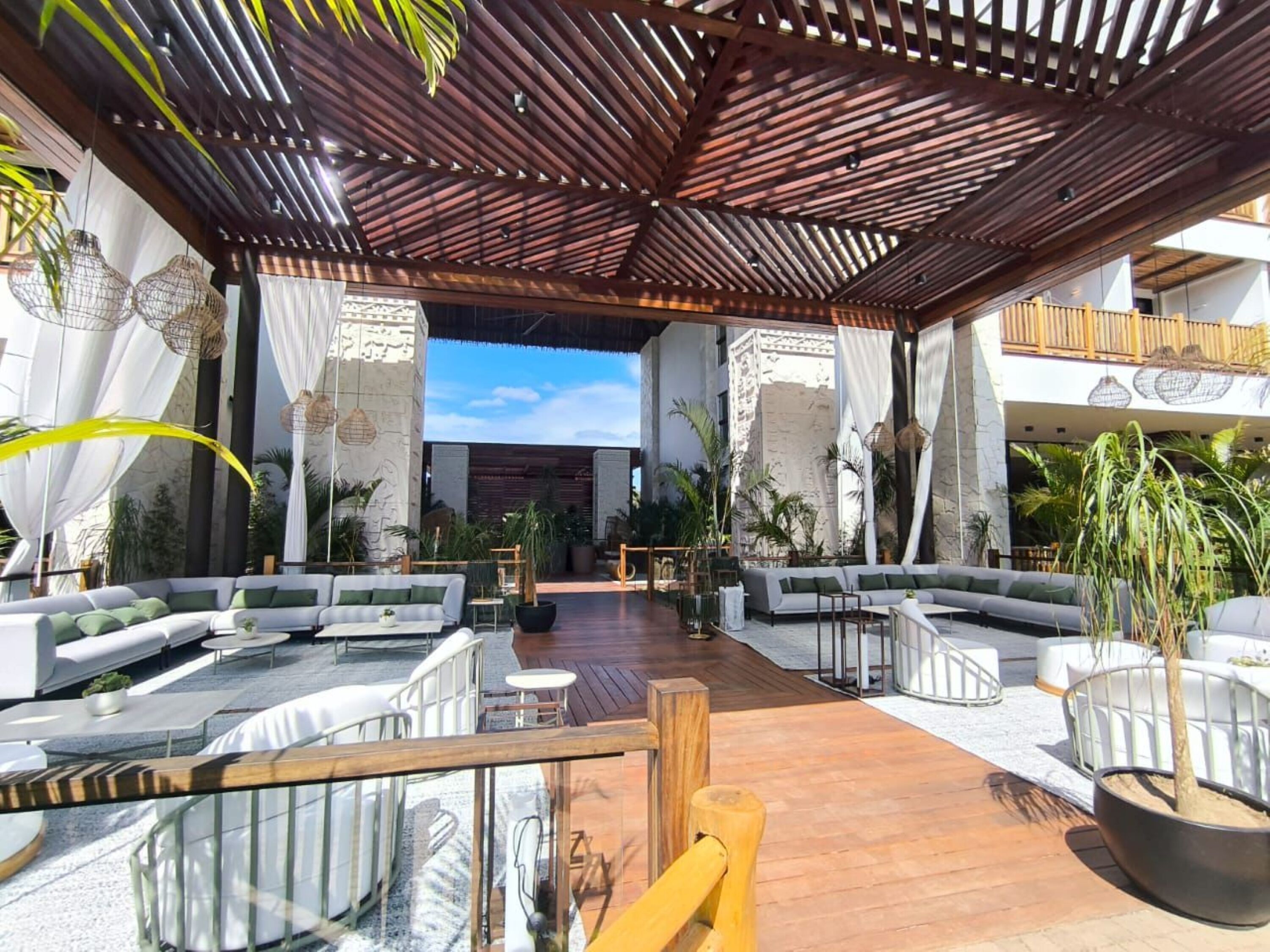 An outdoor lounge area with multiple seating arrangements, including sofas and chairs, under a wooden pergola.