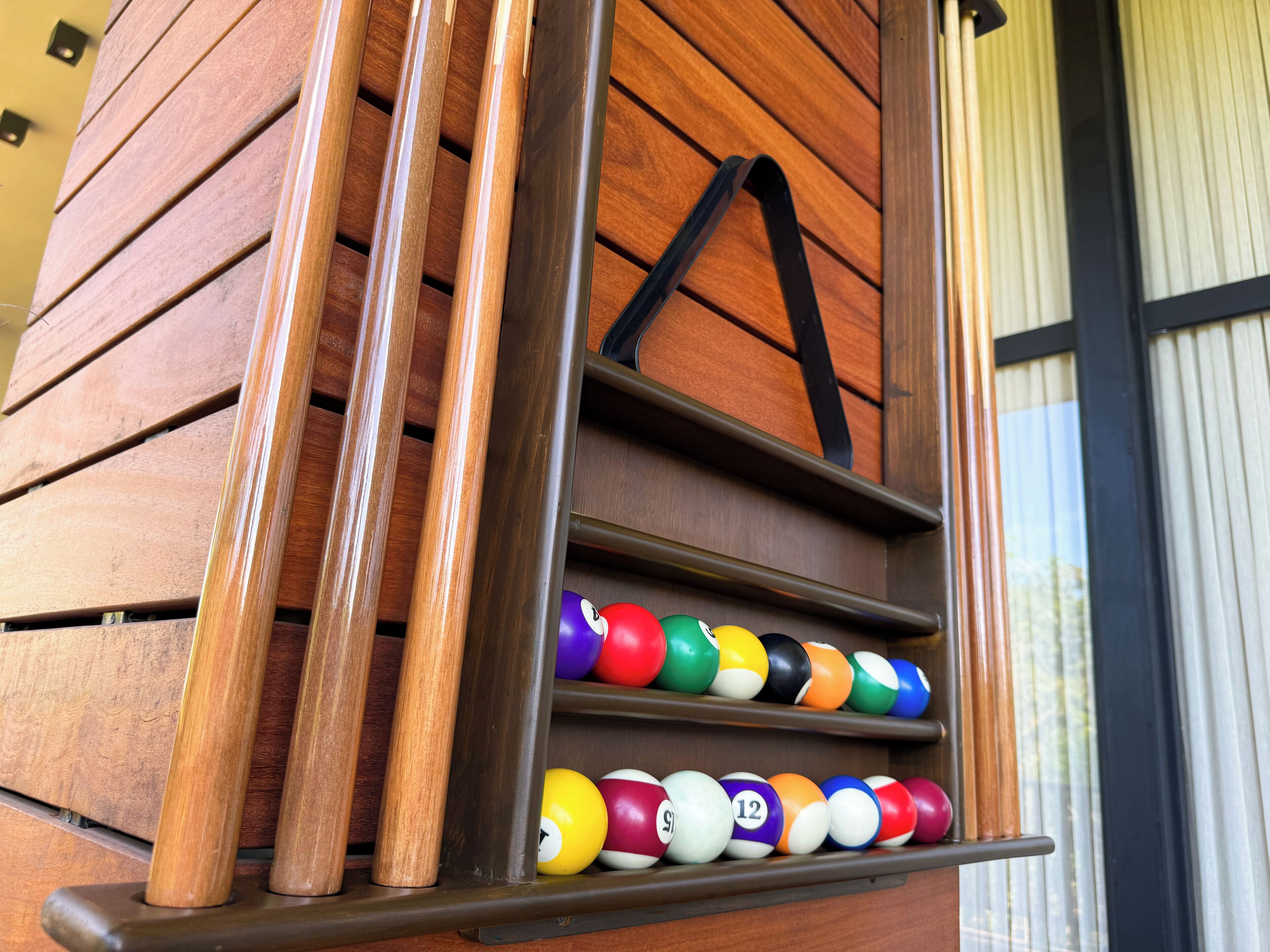 A wooden wall with a shelf holding colorful pool balls.