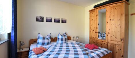 Ein Schlafzimmer mit karierter Bettdecke, einem Holzschrank und einem Nachttisch mit Lampe.