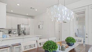 Una cocina moderna con armarios blancos, una mesa de comedor de madera y una lámpara colgante.