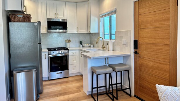 Una cocina moderna con armarios blancos, un refrigerador de acero inoxidable, una estufa a gas y una puerta de madera.