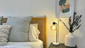 Una cama bien hecha con cabecera de madera, una mesita de noche con lámpara y un cuadro colgado en la pared.