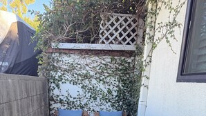 Una pequeña zona de estar al aire libre con una mesa de madera y dos bancos acolchados, rodeada por un muro blanco y una cerca de madera.