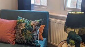 Une pièce avec un canapé bleu, des coussins à motifs léopard et à motifs de feuilles, une lampe sombre et une petite plante.
