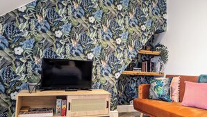 Un salon avec un téléviseur à écran plat posé sur un meuble en bois, une bibliothèque et un canapé agrémenté de coussins colorés.