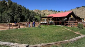A rustic lodge with a red roof, wooden fences, and a mountainous backdrop. - River's Edge Retreat: Your Launchpad for Colorado's Outdoor Wonders (Almont)