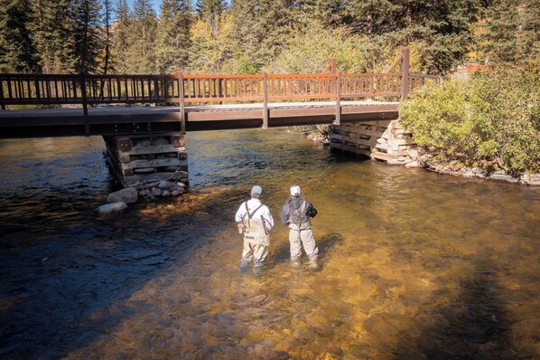 A wooden bridge over a clear stream with two people standing in the water.