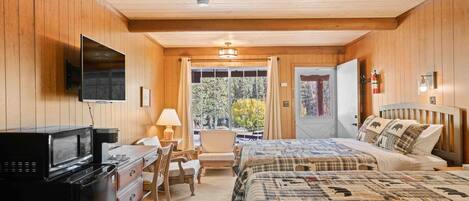 Um quarto aconchegante com paredes de madeira, uma cama com colcha xadrez, uma escrivaninha com micro-ondas e uma TV na parede.