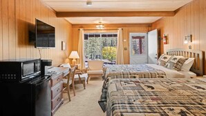 A cozy room with wooden walls, a bed with a plaid quilt, a desk with a microwave, and a TV mounted on the wall. - Fly Fish Paradise: Pet-friendly Cabins with Horseback Riding and ATV Trails (Almont)