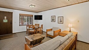 Une pièce avec un plafond en bois, un téléviseur fixé au mur, un canapé en bois, une table basse en bois, une chaise en bois et une lampe sur une table d’appoint.