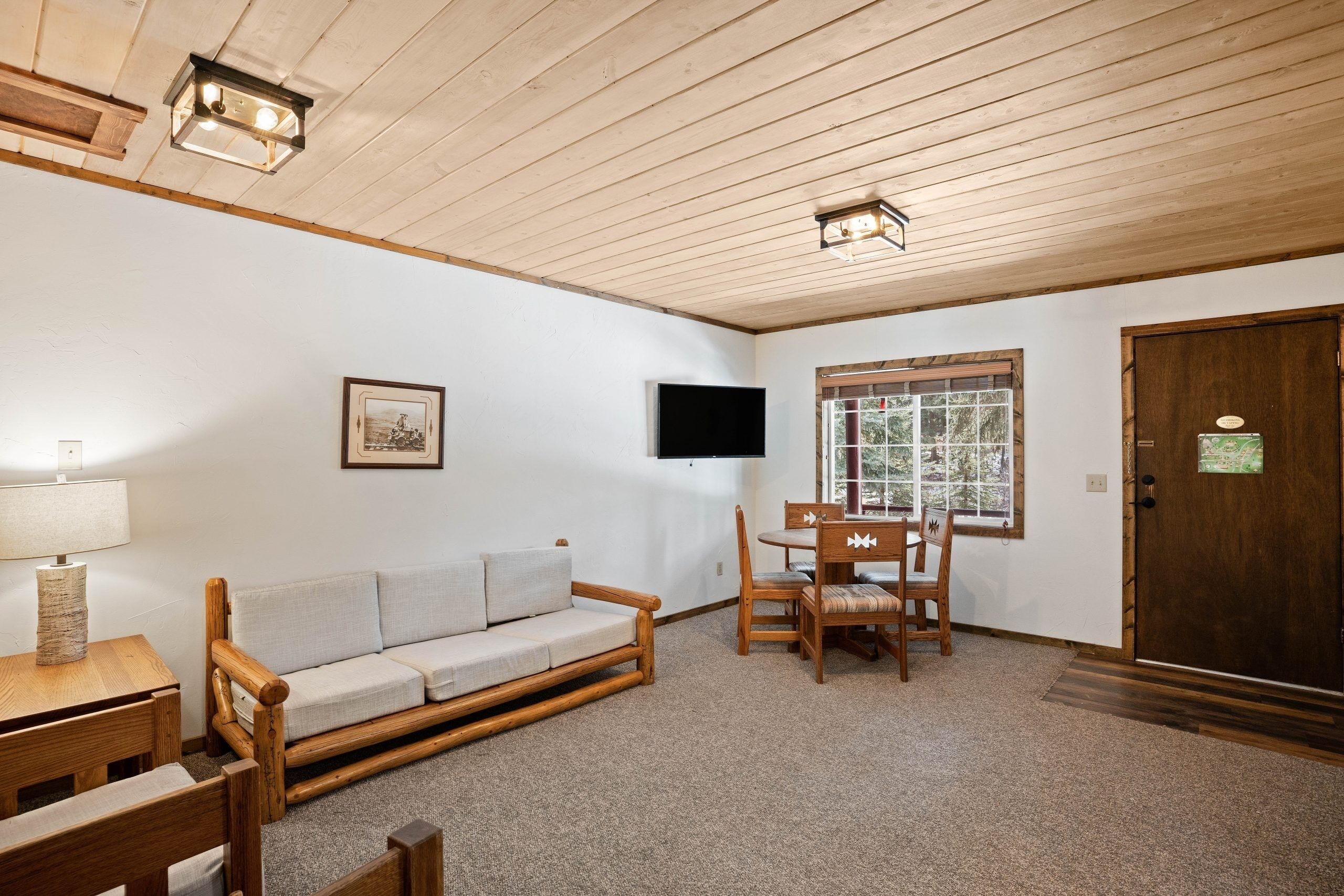 Una stanza accogliente con soffitto in legno, un divano, un tavolo da pranzo con sedie, un televisore a parete e una porta con finestra.