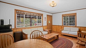 A cozy room with wooden walls, a round table, two sofas, and large windows offering a view of greenery. - Outdoor Enthusiast's Haven: Fish, Raft & Ride in Colorado's Wilderness (Almont)