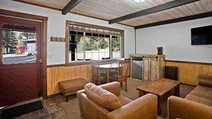 Una habitación con techo de madera, una puerta roja, una ventana con persianas, una mesa de madera y sofás de cuero.