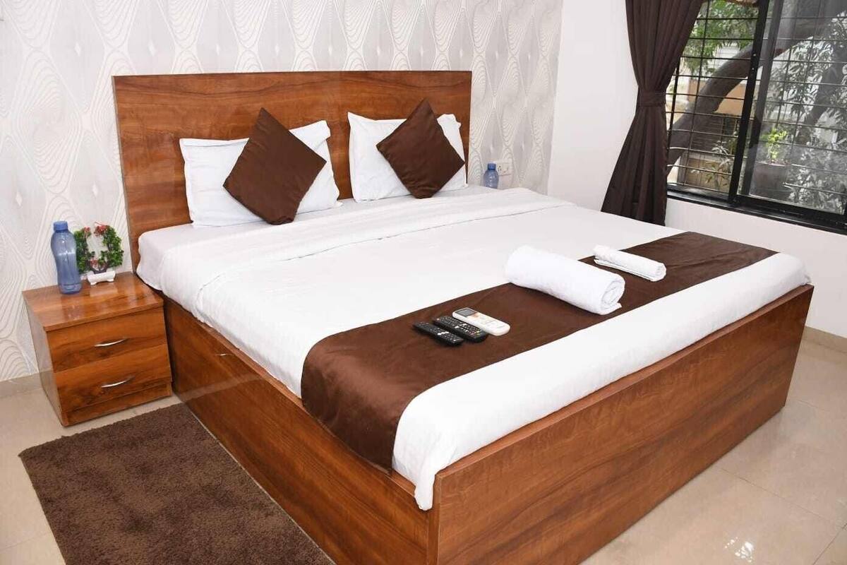A neatly made bed with a wooden headboard, white bedding, and brown pillows. There is a remote control and a rolled towel on the bed.