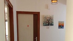 A hallway with a door marked '2', a tiled floor, a light fixture, and two paintings on the wall. - Tulsi Home Stay (Mumbai)