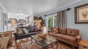A spacious living room with a brown leather sofa, a black leather sofa, and a patterned rug. There is a dining area in the background with a wooden table and chairs.