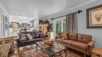 A spacious living room with a brown leather sofa, a black leather sofa, and a patterned rug. There is a dining area in the background with a wooden table and chairs.