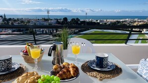 A balcony table with breakfast items, a view of a sports field, and a cityscape. - Apartment Mar de Nerja Sunset (Nerja)